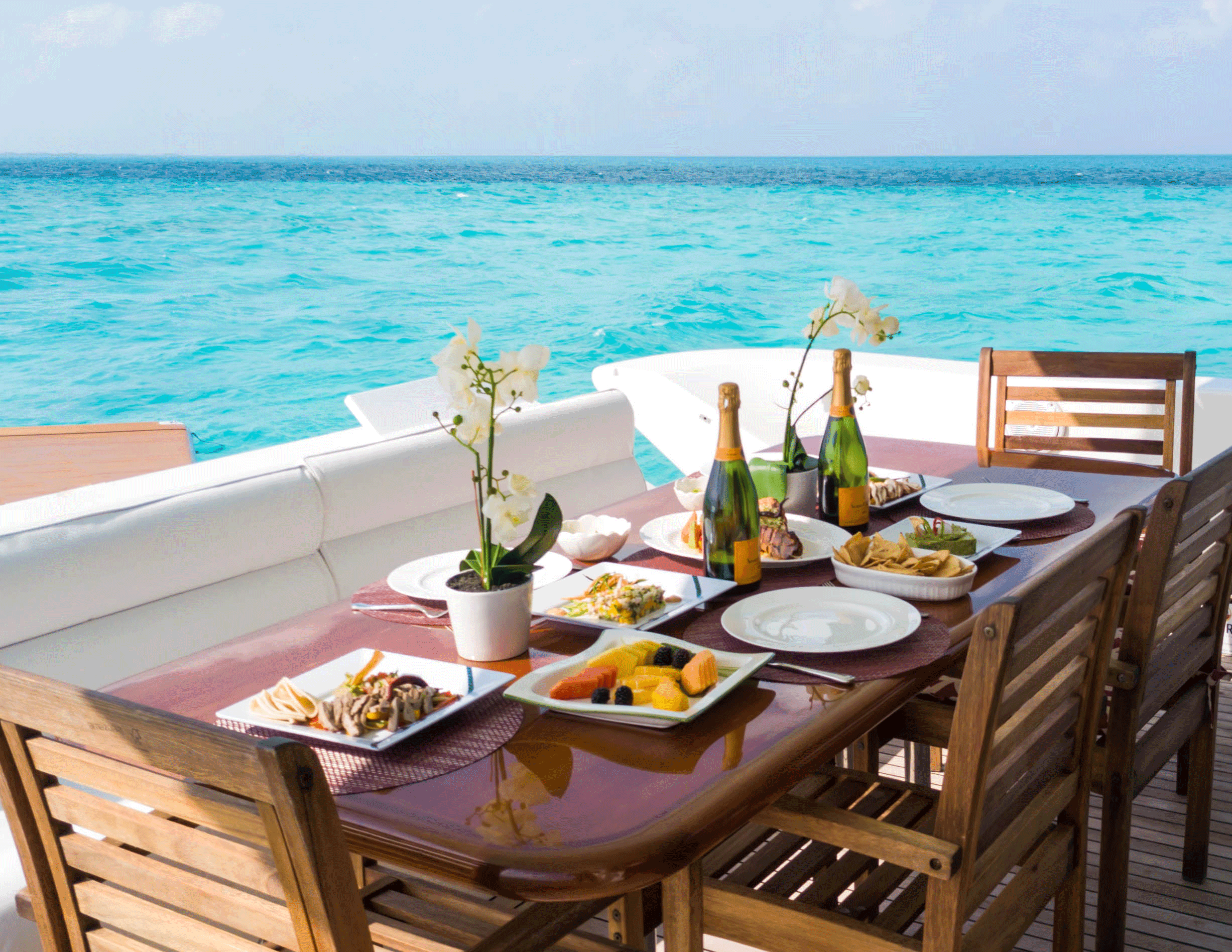 Mesa de lujo a bordo con champagne, orquídeas y el Caribe turquesa